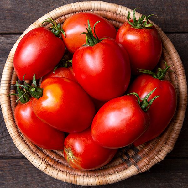 Fresh ripe red Roma tomatoes in a rustic wicker basket. Delicious garden produce for healthy cooking.