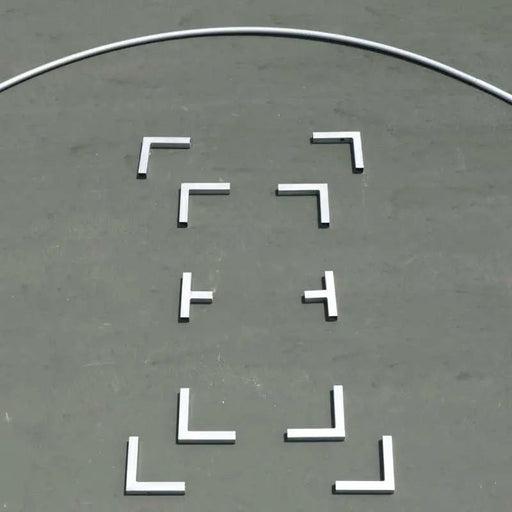 White L-shaped and T-shaped training markers on a grey sports court surface with a curved boundary line.
