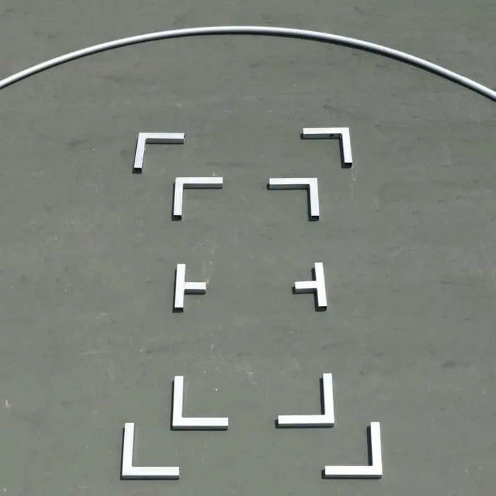 White L-shaped and T-shaped training markers on a grey sports court surface with a curved boundary line.