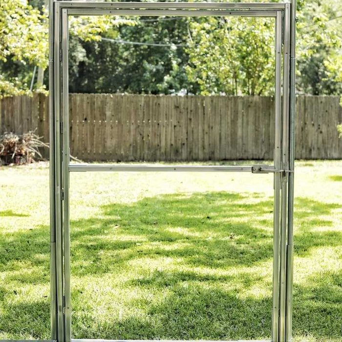 Aluminum greenhouse door frame with latch, clear view of a green backyard lawn and wooden fence.