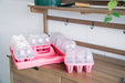 Pink seed starting trays and mini greenhouses on a wooden potting bench. Gardening tools and plant vine visible.