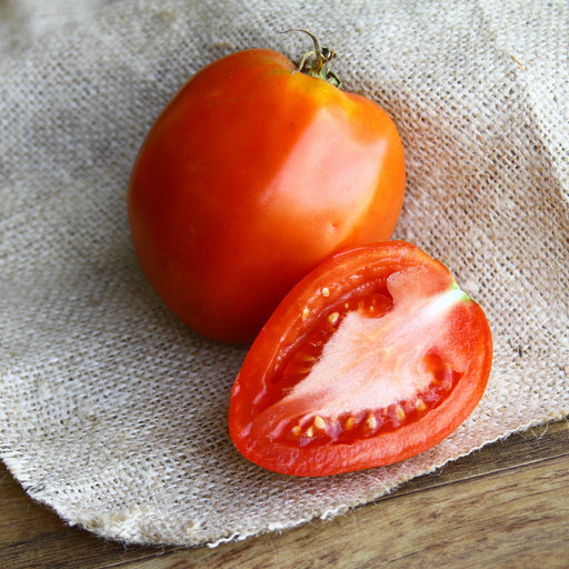 Whole ripe red tomato and a sliced half on a rustic burlap surface. Fresh, organic, healthy produce.