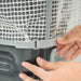 Hands fastening a clear, grid-reinforced washing machine cover with an adjustable grey strap for appliance protection.