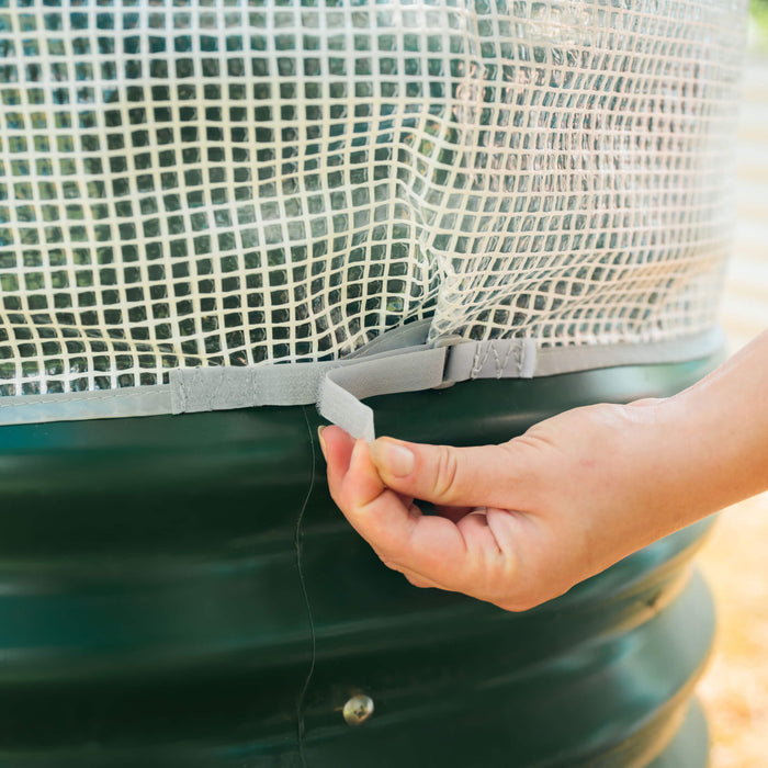 Hand securing reinforced clear cover with velcro strap to a green compost bin.