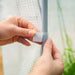 Hands securing a translucent greenhouse cover to a frame pole with a white Velcro strap. Garden setup.