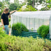 Woman tending green corrugated raised garden bed with white hoop house cover, growing fresh herbs.