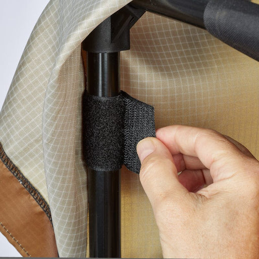 Hand securing beige ripstop fabric to a black tent pole with a hook-and-loop strap. Camping gear assembly.