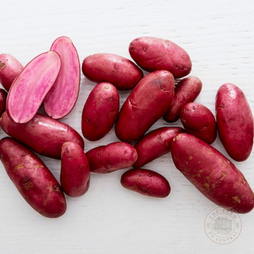 Vibrant red potatoes, some halved to show their bright pink flesh, scattered on a white surface.