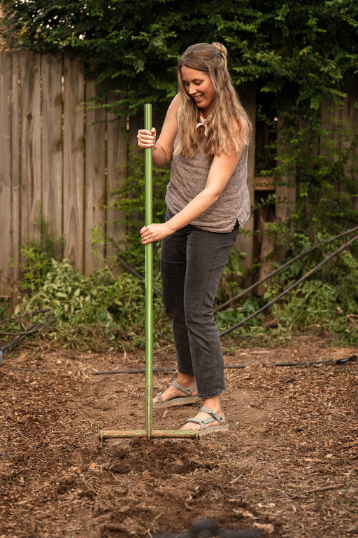 Smiling woman gardener preparing soil with green hoe in backyard garden bed.