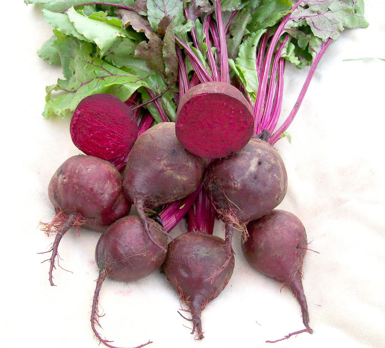 Fresh whole and halved beets with green tops, revealing vibrant red flesh. Healthy root vegetables.