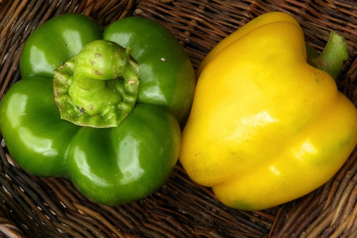 Fresh green and yellow bell peppers in a rustic woven basket.