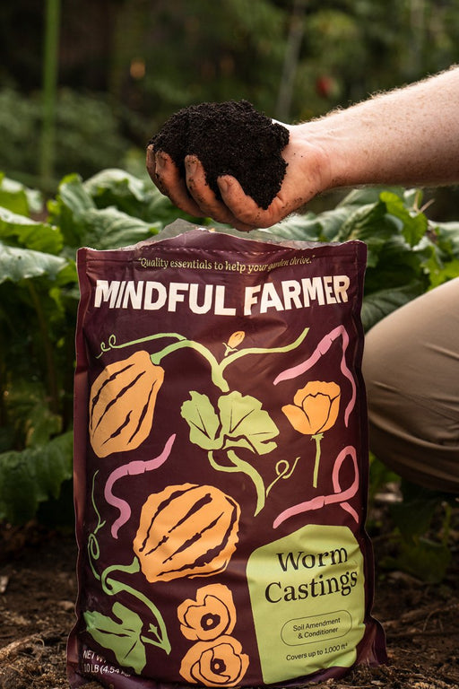 Organic worm castings held in a hand over a Mindful Farmer bag, ready for garden soil amendment.