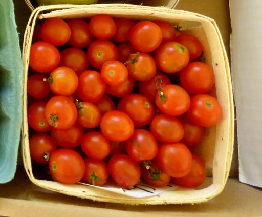 Ripe, vibrant red cherry tomatoes with green stems, packed tightly in a rustic wooden basket. Fresh garden produce.